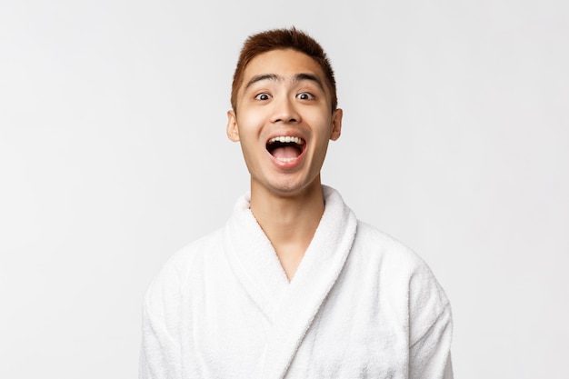 Portrait of young Asian man in bathrobe showing gesture. After shower