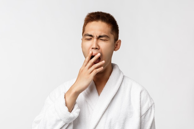 Portrait of young Asian man in bathrobe showing gesture. After shower