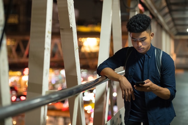 Portrait of young Asian man on the footbridge in the city at night