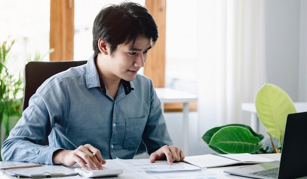 若いアジア人男性の肖像フリーランサーは、現代のオフィスでコンピュータータブレットに取り組んでいます会計分析レポートを行う不動産投資データ金融および税制conceptxA