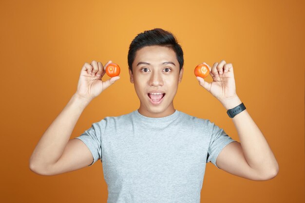 Portrait of young Asian man holding two tomatoes behind his ears