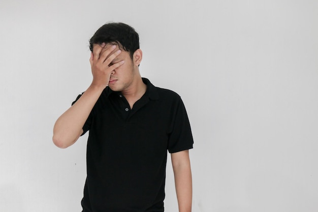 Portrait of young asian man isolated on grey background suffering from severe headache pressing fingers to temples closing eyes to relieve pain with helpless face expression