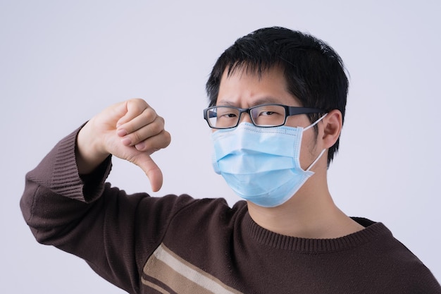 Portrait of young asian man saying no to coronavirus infection\
with wearing medical surgical blue face mask isolated on white\
background close up closeup