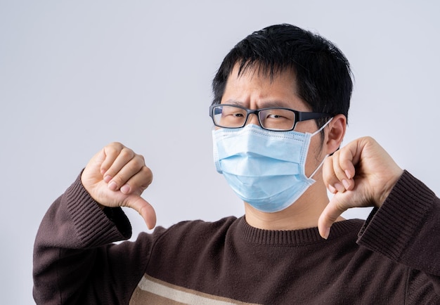 Portrait of young Asian man saying no to coronavirus infection with wearing medical surgical blue face mask isolated on white background close up closeup