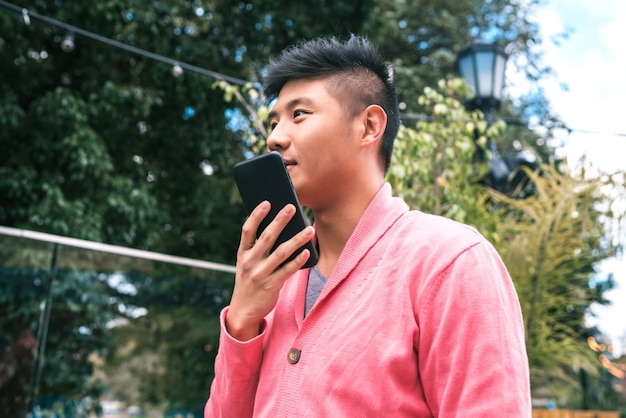 Portrait of young Asian man sending a voice message on the phone outdoors in the street.