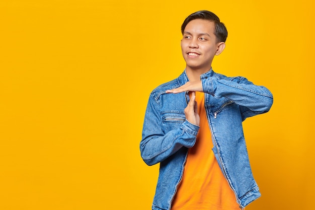 Portrait of young asian man showing timeout gesture on yellow background