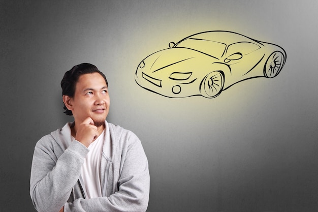 스포츠 자동차 를 소유 하는 꿈 을 꾸고 미소 짓는 젊은 아시아인 의 초상화