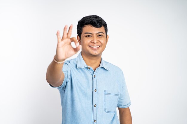 孤立した背景に大丈夫な手のジェスチャーで立つ若いアジア人男性の肖像画