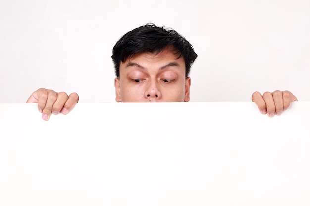 Portrait of young asian man standing behind an empty signboard and glancing on it