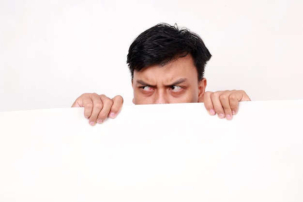 Portrait of young asian man standing behind an empty signboard and looking sideways