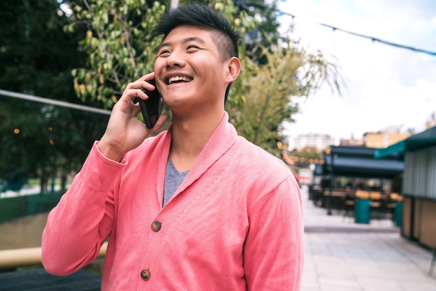 Portrait of young Asian man talking on the phone outdoors in the street. Communication concept.