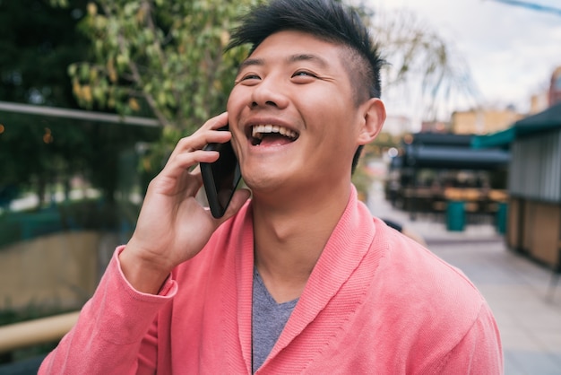 Portrait of young Asian man talking on the phone outdoors in the street