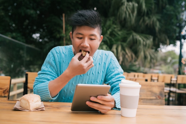 コーヒーショップに座っているときに彼のデジタルタブレットを使用して若いアジア人の肖像画。