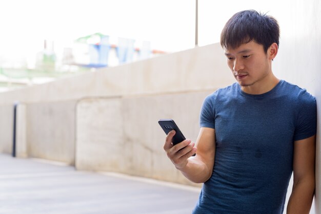 Photo portrait of young asian man using phone in the city outdoors