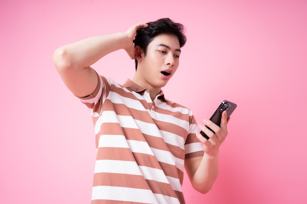 Portrait of young Asian man using smartphone on pink background