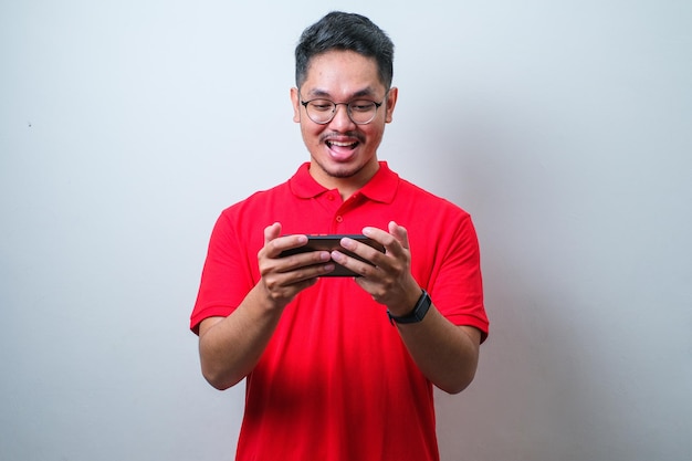 Portrait of young Asian man wearing casual shirt playing online game on mobile phone