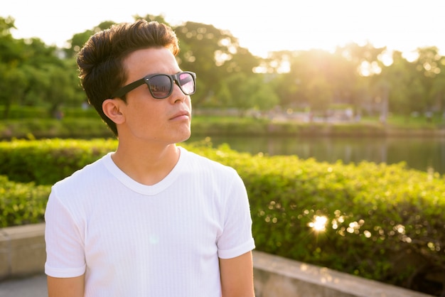 Portrait of young Asian man wearing sunglasses while relaxing at the park in Bangkok, Thailand