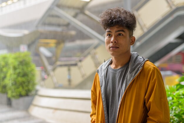 Portrait of young Asian man with curly hair in the city outdoors with rain