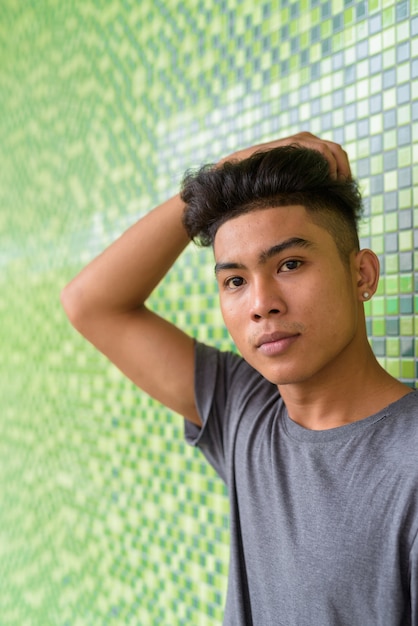 Portrait of young Asian man with curly hair on green tiled wall