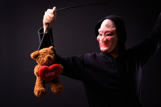 Portrait of young asian man with hoodie and horror mask on black