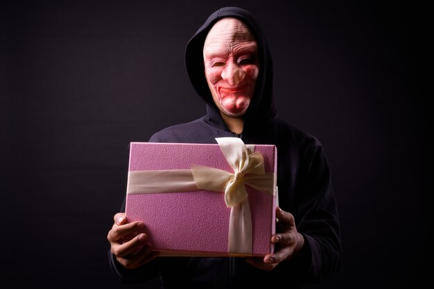 portrait of young Asian man with hoodie and horror mask on black