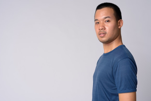 Portrait of young Asian man with short hair against white wall