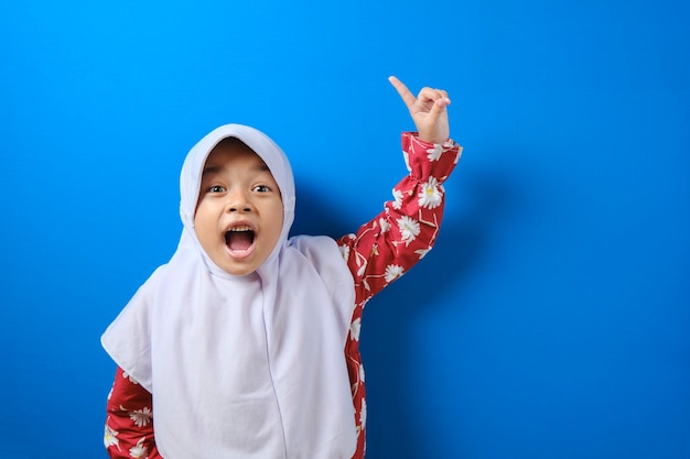 Portrait of young Asian muslim girl looked happy, thinking and looking up, having good idea. Half body portrait against blue background with copy space