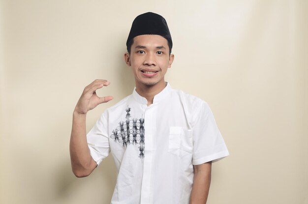 Photo portrait of young asian muslim man showing small size with his hands isolated background