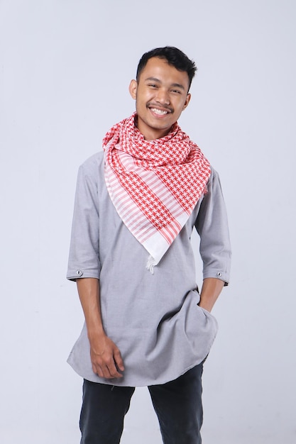 Portrait of a young Asian Muslim man wearing religious clothing and scarf in white background.