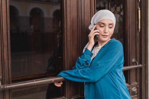 屋外で携帯電話で話している若いアジアのイスラム教徒の学生女性の肖像画