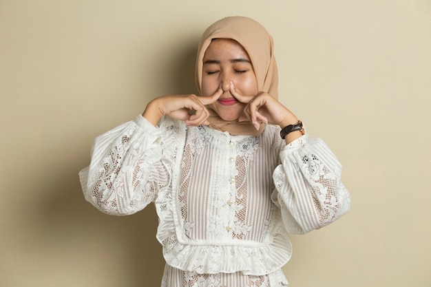 Portrait of young Asian muslim woman wearing hijab  holding her nose because of a bad smell