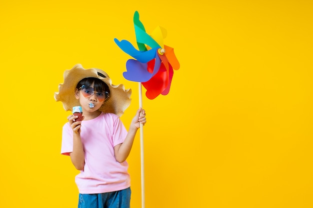 Portrait of young Asian pretty girl holding colorful turbine and eating ice cream on yellow