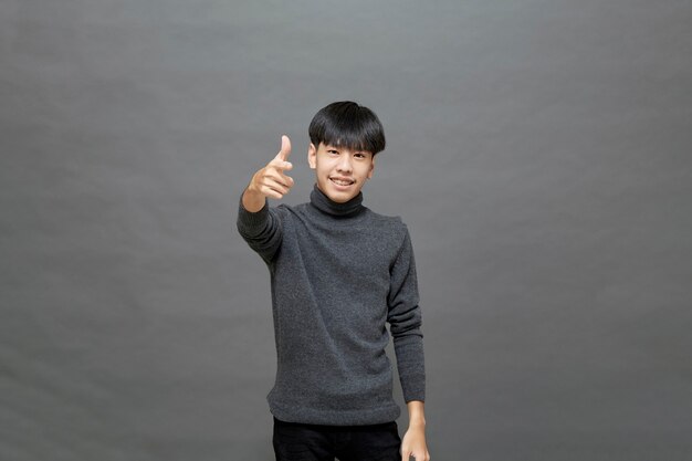 Portrait of Young Asian teenage cool hair stylish wearing grey sweater pointing finger studio shot isolated on gray background