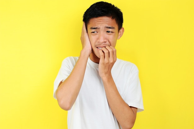 Portrait of young Asian teenager unhappy scared man, isolated on yellow background