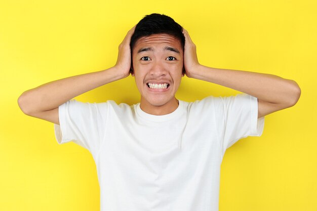 Ritratto di giovane adolescente asiatico infelice uomo spaventato, isolato su sfondo giallo