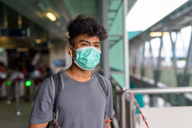 Portrait of young Asian tourist man as backpacker with mask for protection from coronavirus outbreak at the sky train station