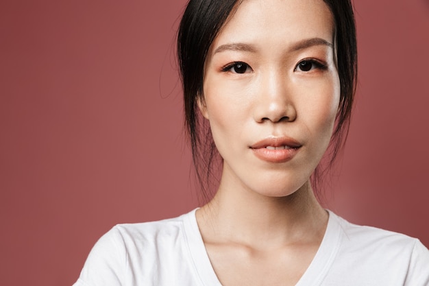 Portrait of young asian woman dressed in basic wear  with lovely glance isolated over red wall