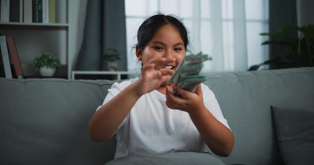 Portrait of a young Asian woman enjoying scattering cash bills on a sofa in the living room at home