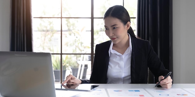 Portrait of young asian woman hand freelancer is working her
job on computer tablet in modern office doing accounting analysis
report real estate investment data financial and tax systems
concept