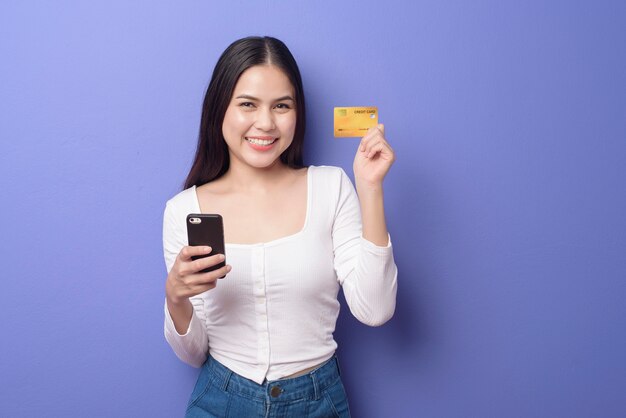 Portrait of Young Asian woman is using cell phone with credit card on purple background