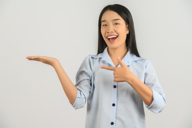 Портрет молодой азиатки, указывающей двумя руками и пальцами в сторону на изолированном белом фоне