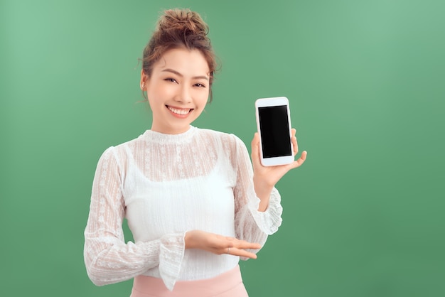 Portrait of young Asian woman showing her blank sreen mobile phone. Isolated over green background.