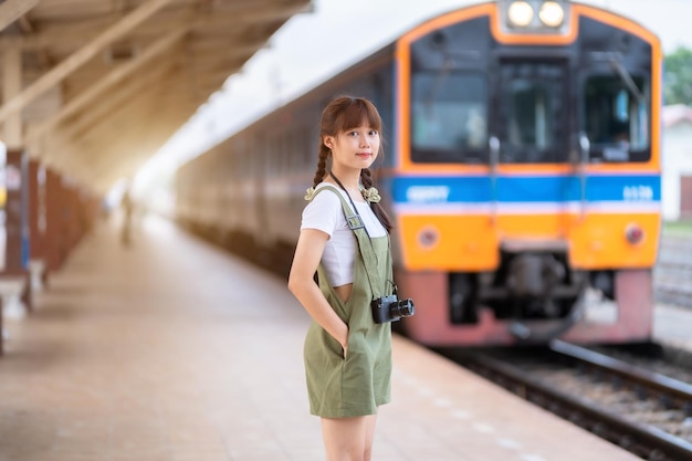 Portrait Young asian woman smiling tourist Traveler girl walking and with a holding the camera waits train travel journey is taken in railway platform Thailand summer relax vacation Concept