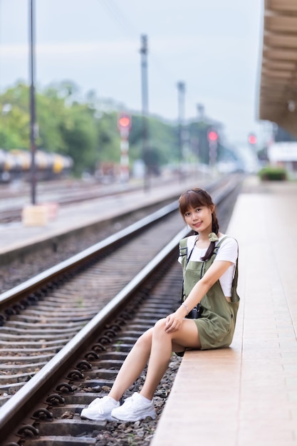 Portrait Young asian woman smiling tourist Traveler girl walking and with a holding the camera waits train travel journey is taken in railway platform Thailand summer relax vacation Concept