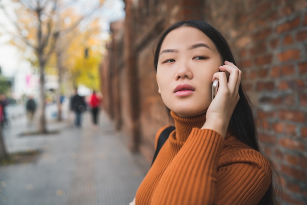 Portrait of young Asian woman talking on the phone outdoors in the street.