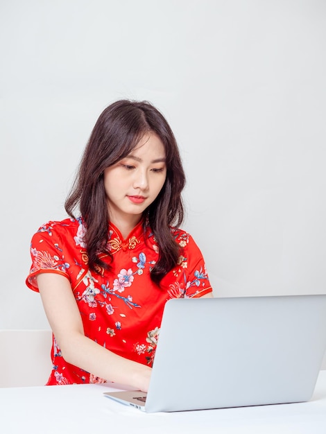 Photo portrait of a young asian woman in traditional cheongsam qipao dress using laptop on white background