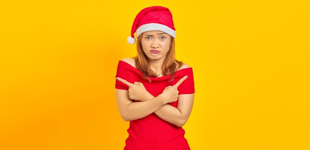 Portrait of young Asian woman wearing Christmas hat pointing to copy space with finger and having doubts