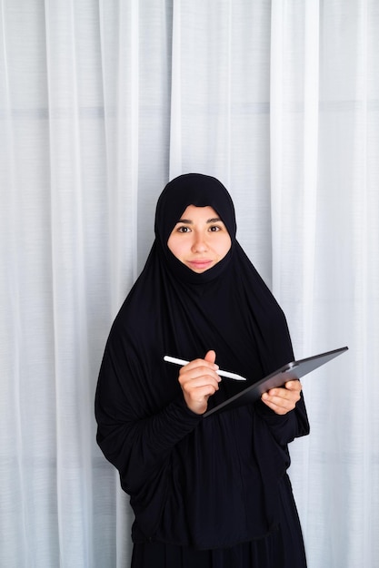 Portrait of young asian woman wearing hijab, working at home\
with tablet