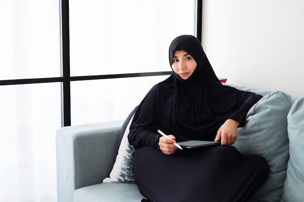 태블릿 집에서 일하는 hijab를 착용하는 젊은 아시아 여자의 초상화