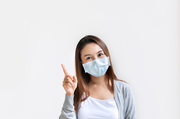 Portrait of young Asian woman wearing  protective mask pointing with index finger upwards